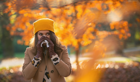 Donna in un bosco in autunno si soffia il naso a causa delle allergie autunnali