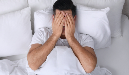 Uomo a letto si copre gli occhi con le mani a causa della secchezza oculare al risveglio